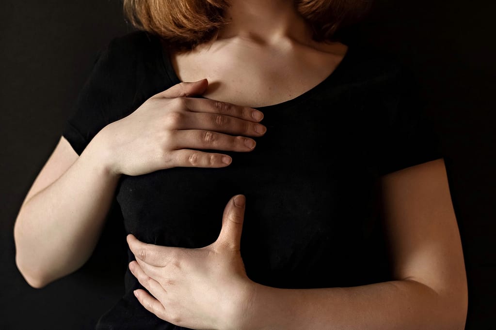 A girl in a black t-shirt clasps her chest with both hands.The concept of breast cancer.